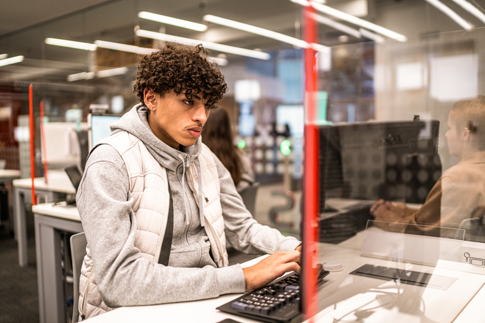 Et foto af en universitetsstuderende, der studerer ved en stationær PC i et computerrum.