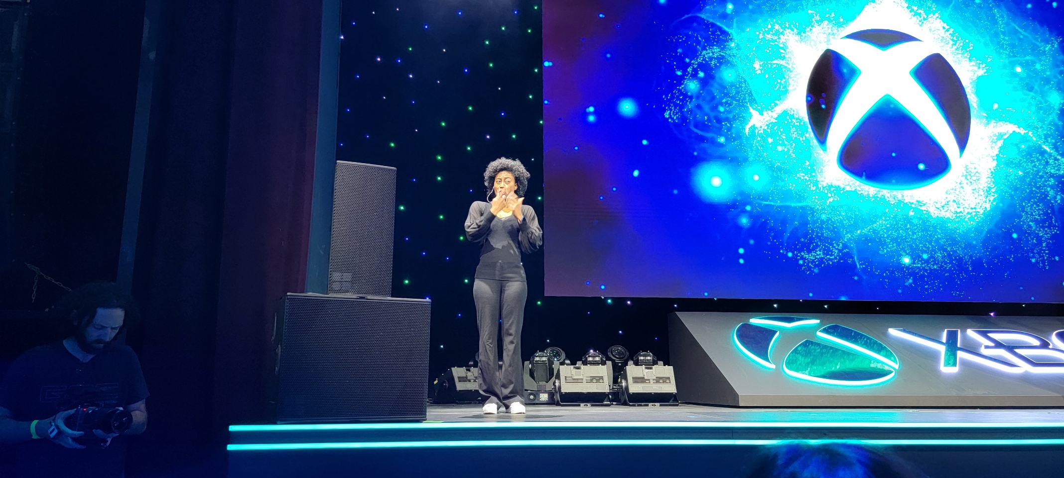 A woman stands on a stage, signing. Behind her and Xbox logo is projected on a screen.