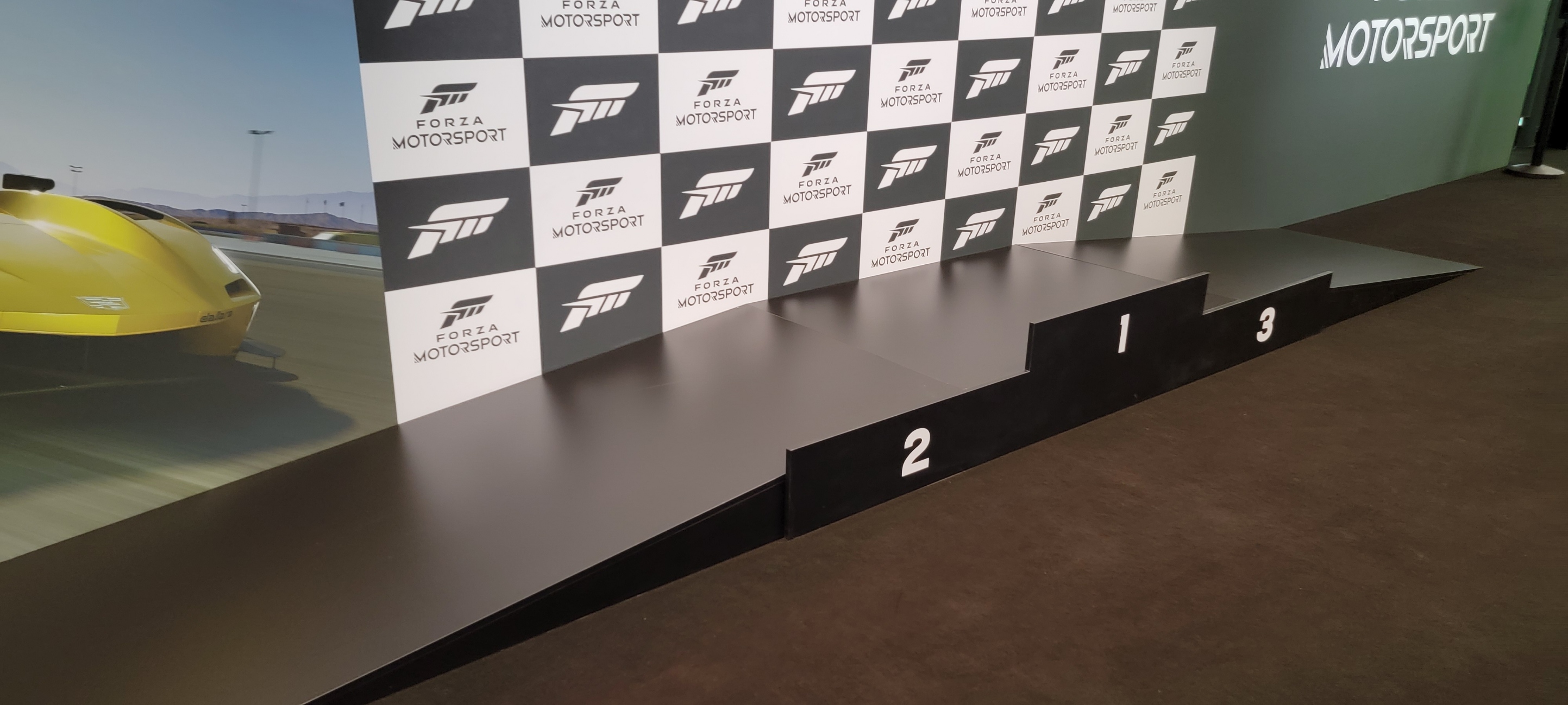 A podium with places for 1st, 2nd, and 3rd place winners to stand, with a checkered background. A ramp is attached.