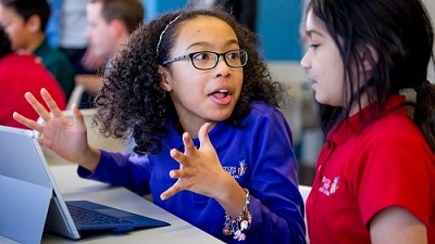 Photo of students speaking to each other in front of a Surface computer.