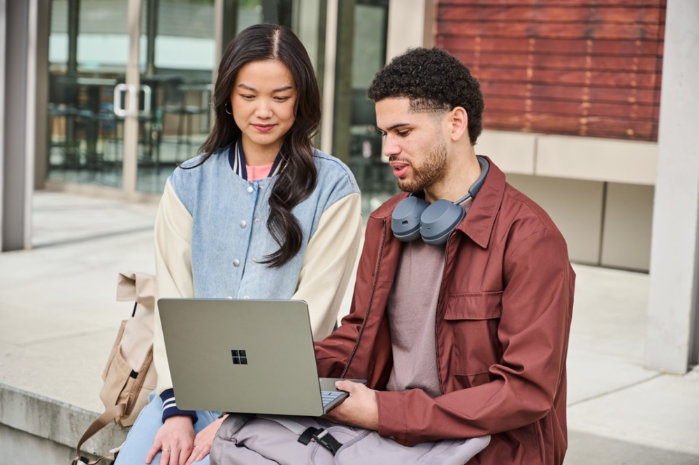 Photo of two people using a laptop outside.