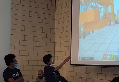 Photo of students pointing to a screen as they present their build to judges.