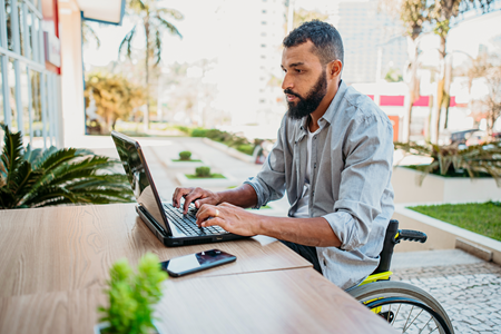 Screenshot of A person working on a computer while sitting at a table outdoors.