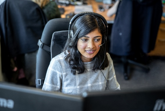 Photo of a woman wearing a headset sitting in front of computer monitors.