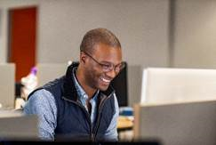 Photo of a man smiling at a computer monitor.