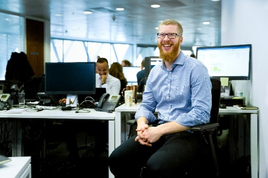 Photo of a man smiling at a camera in a busy office.
