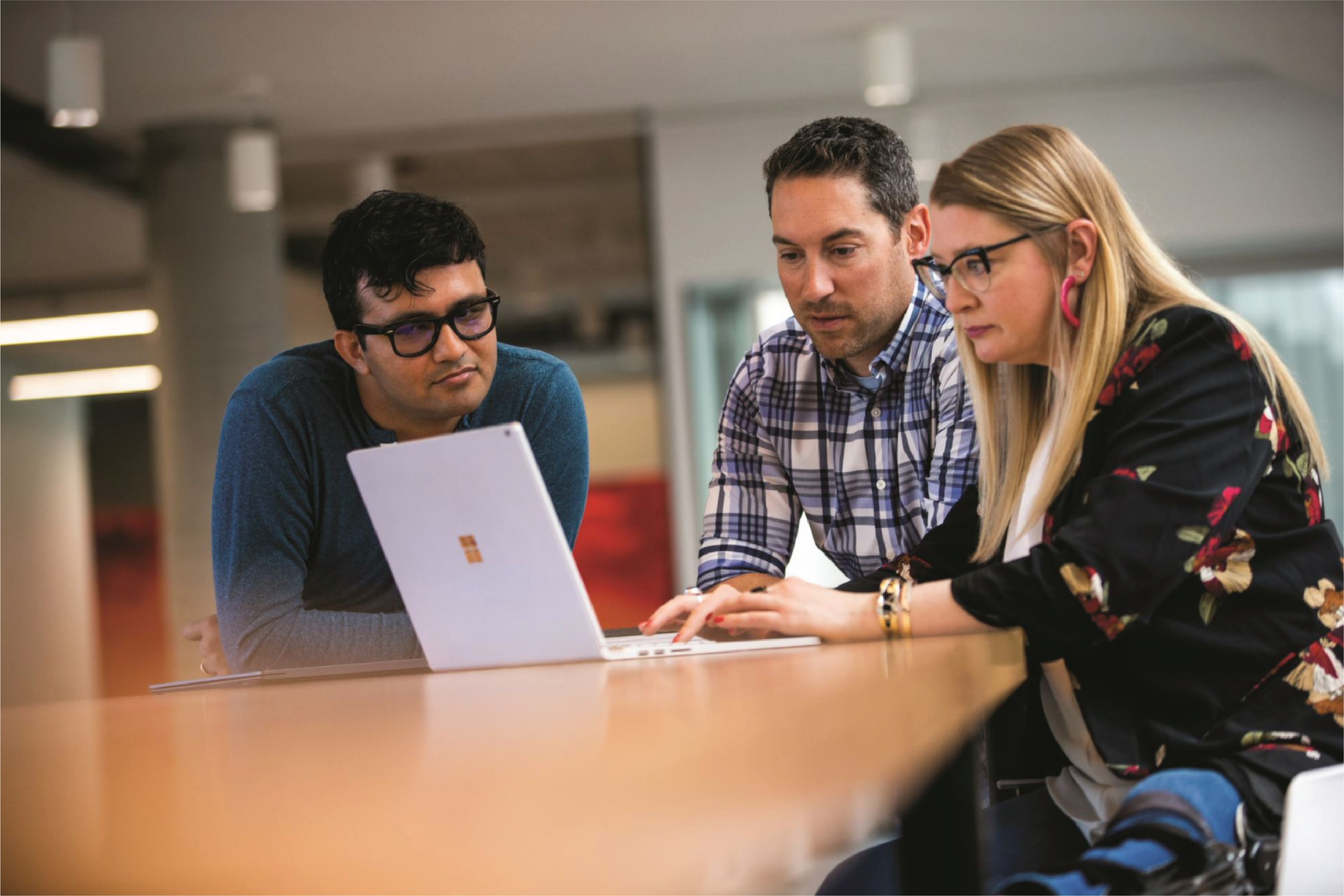 Photograph of two men and a woman sitting together at a table in front of a Microsoft Surface laptop.