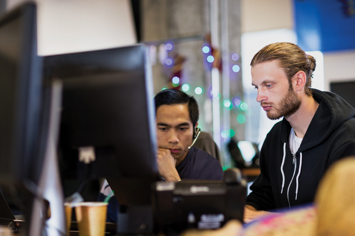 Photo of two people focused on computer screens at a desk.
