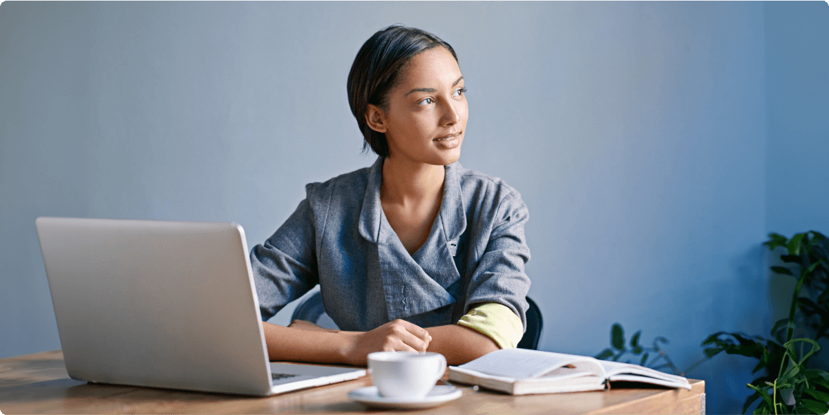 A woman working in a home office with notebooks, laptop and a teacup.