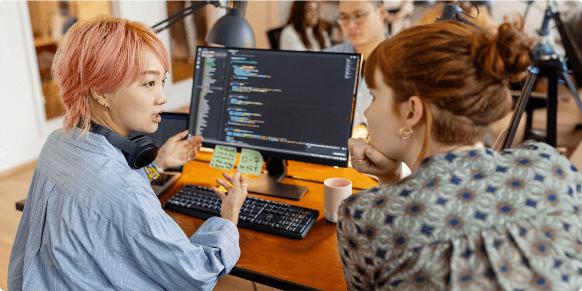 Two women discussing a coding question with each other, in an office.