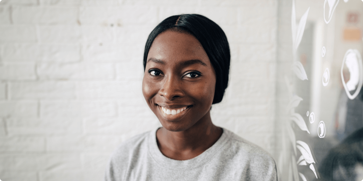 A portrait of a smiling woman in front of a white brick wall.