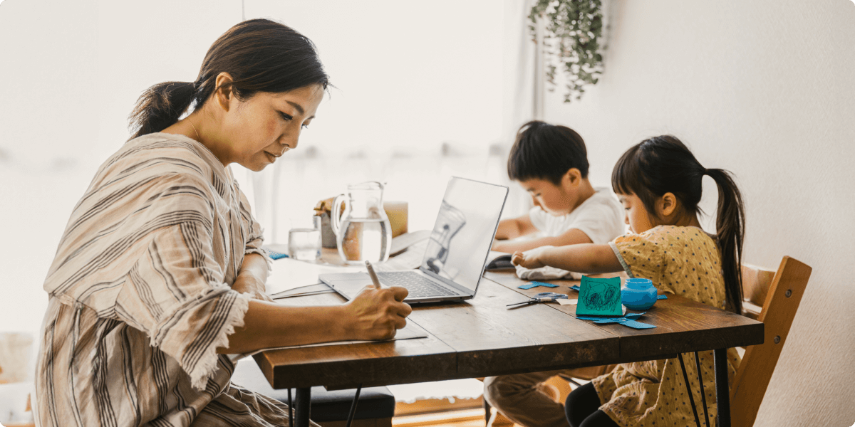 A woman working at the dining room table with her children, who are doing crafts.