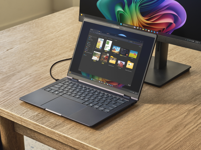 A photograph of a Copilot+ PC and monitor displaying the Windows desktop, positioned on a modern desk.