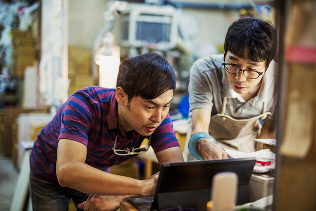 A photograph of two people using a tablet in a workshop surrounded by tools and equipment.