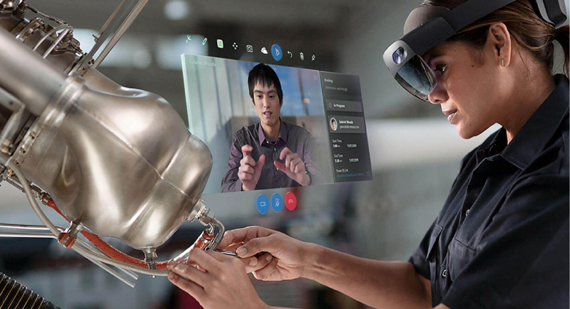Photograph of a HoloLens user performing mechanical repair while using Remote Assist to communicate with a coworker.