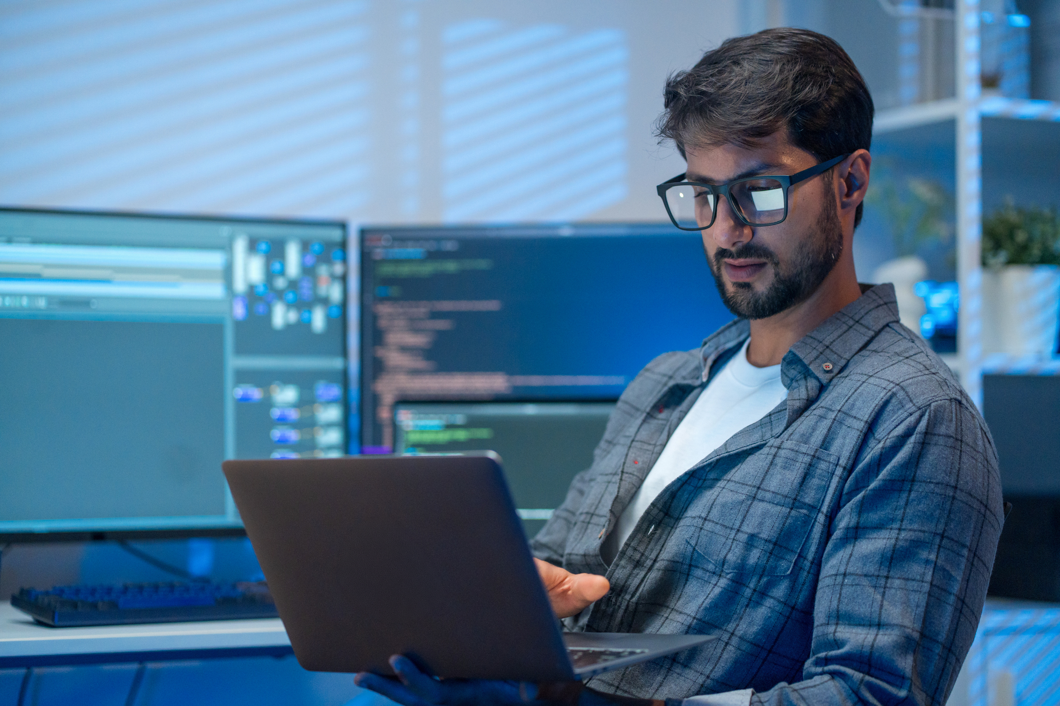 A photograph of a Developer working on a laptop in a modern workspace, with code and development tools visible on external monitors, illustrating how AI capabilities can be integrated into Windows applications using a layered platform approach.