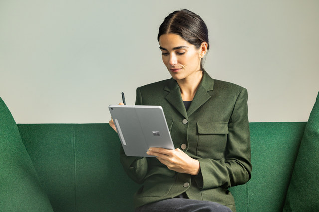 A photograph of a business professional using the Surface Slim Pen 2 on a Surface device while sitting on a couch.