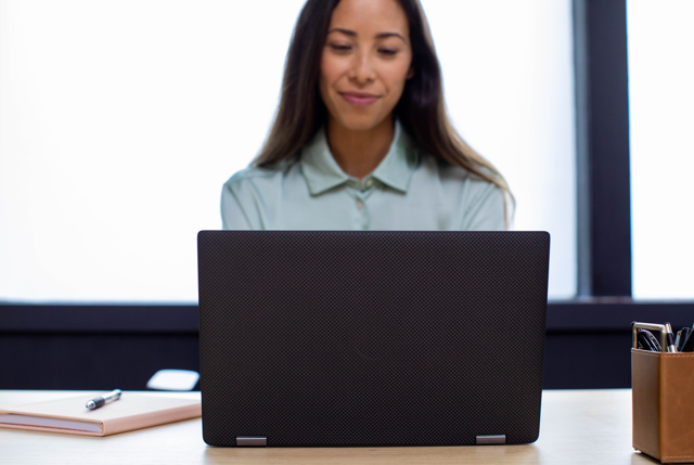 A photograph of a woman working on a laptop at a desk.