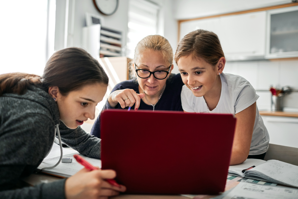 A photo of two students working on a laptop from home with their caretaker.