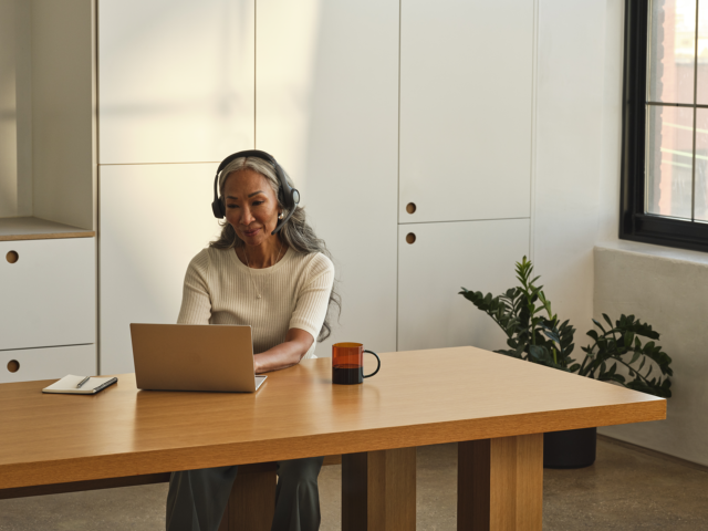 A photograph of a woman working at a desk on a laptop in an office.