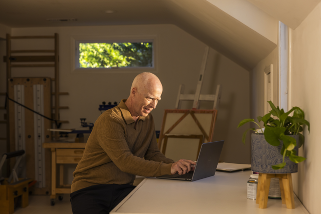 A photograph of a man working from home at a desk on a laptop.