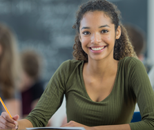 A person smiles as they write with a pencil.