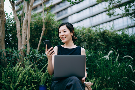 Screenshot of a person working outdoors with a phone and laptop.