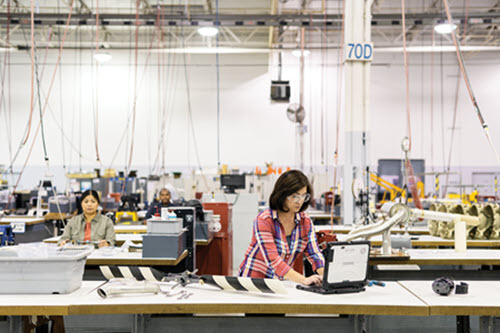 Fotografía que muestra a una mujer en una fábrica trabajando en una mesa usando un ordenador.