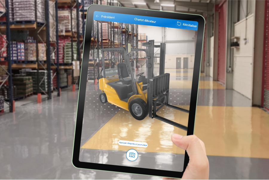 Une photo d’un écran de tablette qui montre un modèle 3D d’un chariot élévateur superposé sur une vue intérieure d’un entrepôt.
