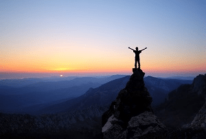 Personne se tenant sur un rocher montagneux au coucher du soleil