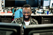 Photo d’un homme arborant un large sourire qui regarde deux écrans d’ordinateur.