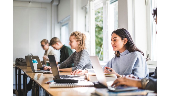 Étudiants assis ensemble à une longue table travaillant sur des ordinateurs portables