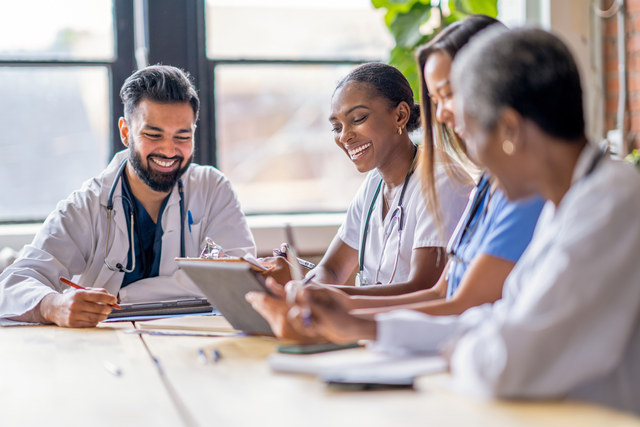 Une photographie de professionnels de la santé parlant autour d’une table avec des tablettes et des papiers.
