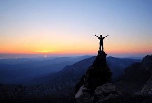 A person standing on a mountain rock at sunset