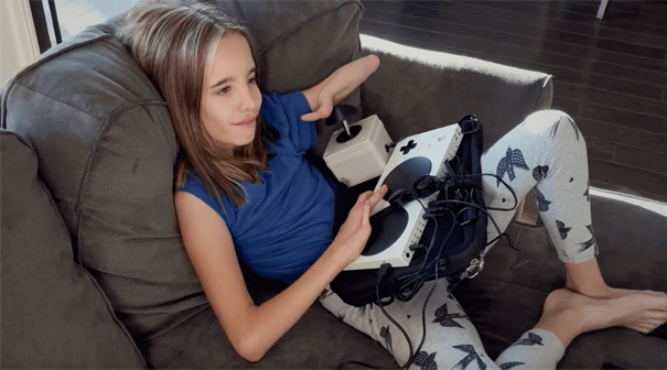 소파에 Xbox 적응형 컨트롤러를 사용하는 이동성 장애가 있는 어린 소녀의 사진.