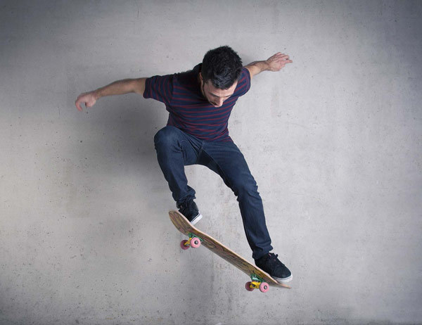 A skateboarder performing a trick in front of a concrete wall.