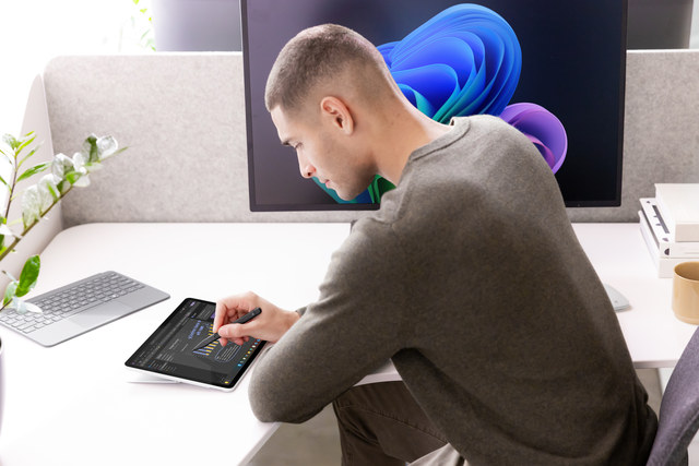 O fotografie cu un profesionist de afaceri așezat la biroul său, folosind un Surface Slim Pen 2 pentru a lucra în OneNote pe dispozitivul lor Surface.