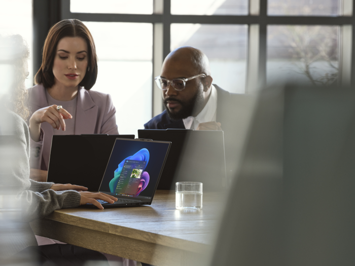 Фотография устройств Windows 11 Pro, используемых командой смешанного пола, сотрудничающей на столе в офисном пространстве.