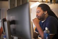 一名男子戴着耳机坐在电脑前的照片。