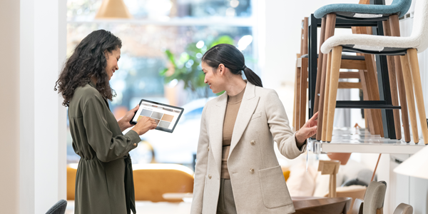 两名妇女站在家具零售店中看着平板电脑。