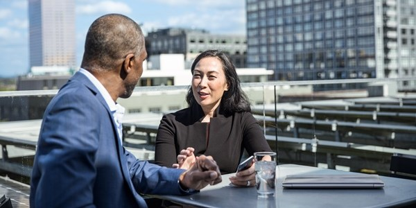 身穿西裝的男女企業上班族坐在屋頂露台。 拿著手機的婦女，桌子上有一台闔上的筆記型電腦。